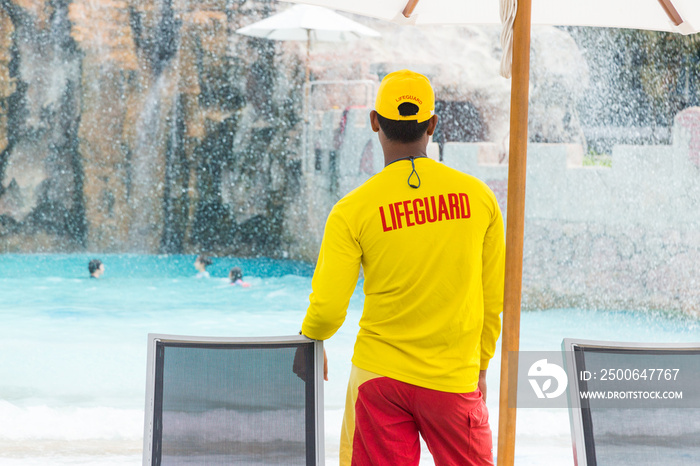 lifeguard man wearing yellow lifeguard shirt and cap, standing on duty
