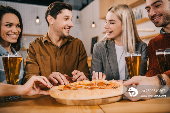 selective focus of cheerful friends taking pieces of tasty pizza in bar