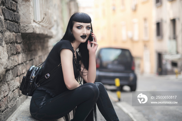 Urban goth girl talking over her cell phone, sitting in an urban outdoor area