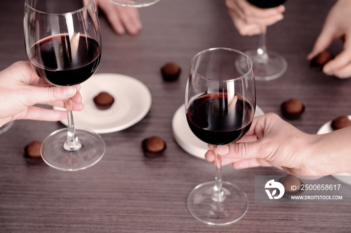 Female hands holding glasses of red wine over wooden table