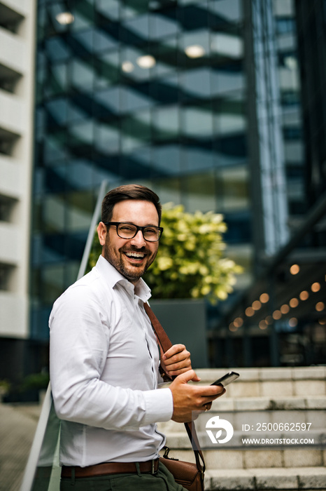 一位微笑的企业家在城市里使用智能手机的肖像。