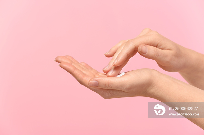 Woman applying body cream onto skin on color background