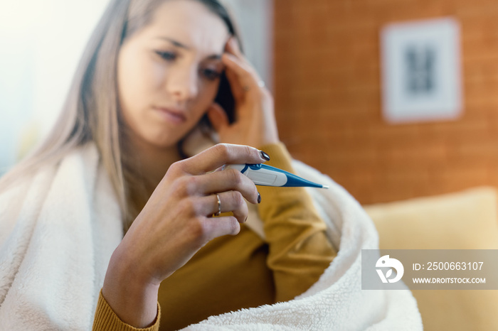 Young woman with cold and flu measuring her temperature