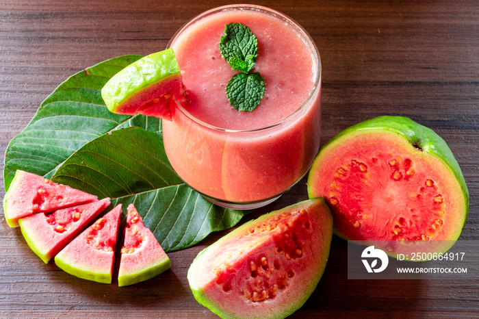 Glass of red guava juice on top of wooden texture, pieces of guava cut in the background