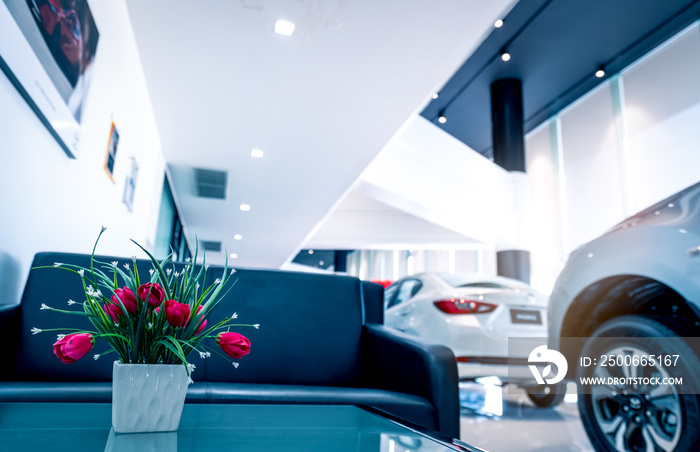 Fake red flowers in vase on table in modern car showroom. Car dealership interior building. Artifici