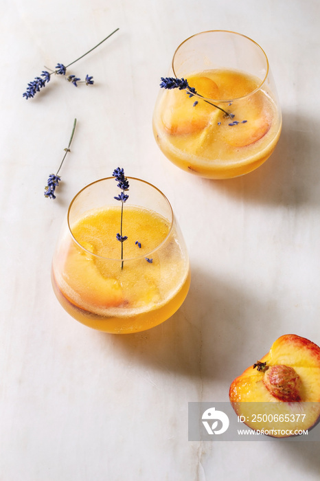 Peach cold lemonade or Bellini cocktail with lavender flowers served in two glasses on white marble 