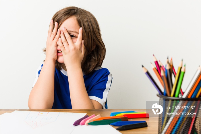 Little boy painting and doing homeworks on his desk blink through fingers frightened and nervous.