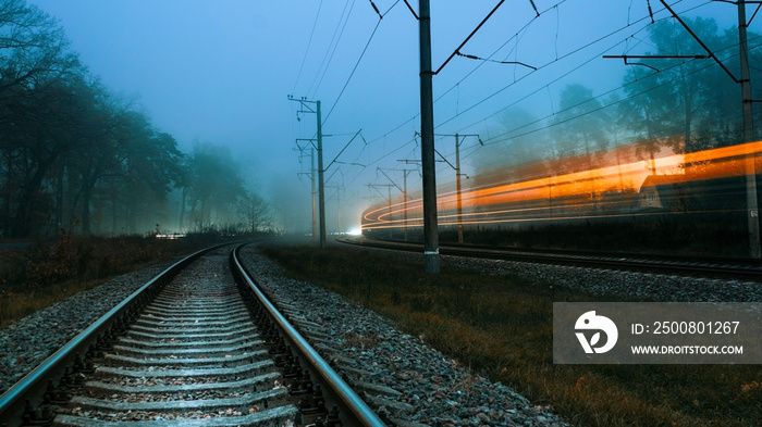 Railroad on a foggy evening. Blurry lights of a passing train. Fast passing train. Gloomy cold evening.