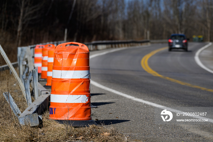 Vehicles drive by a damaged section of guardrail along Rt 79 in Windsor in Upstate NY.  Barrels are placed along the road where an accident recently damaged the guardrail.  Dangerous Curve.