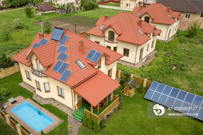 Aerial view of a new autonomous house with solar panels and water heating radiators on the roof and green yard with blue swimming pool.