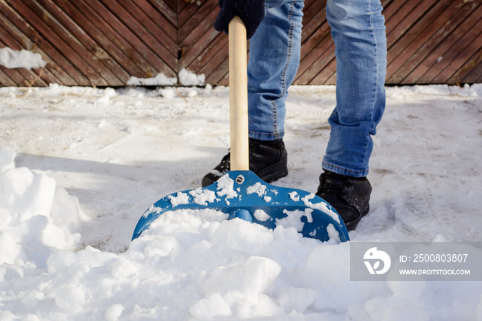 Young man shoveling snow in the driveway near the garage after a heavy snow in order to make way for a car