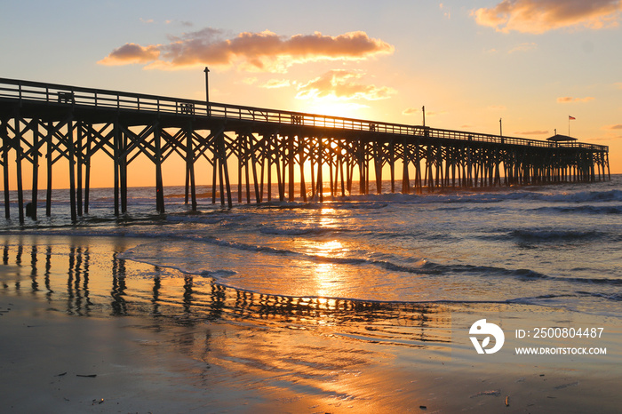 Sunrise at a South Carolina Atlantic coast, Myrtle Beach area, USA. Landscape with the reflection of the sun in shallow water on the foreground and a wooden pier on the background.Vacation background.