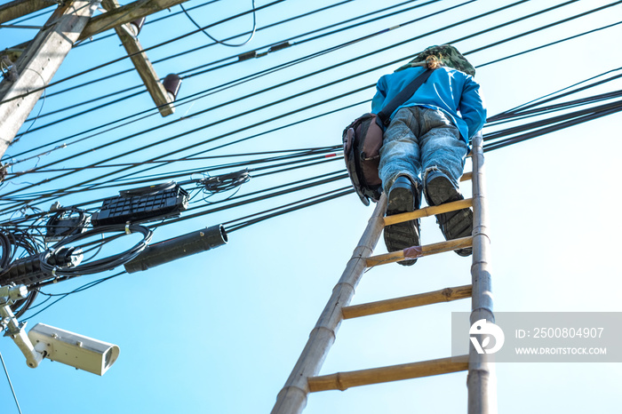 Electrician climbing the bamboo ladder to repair electric wires.