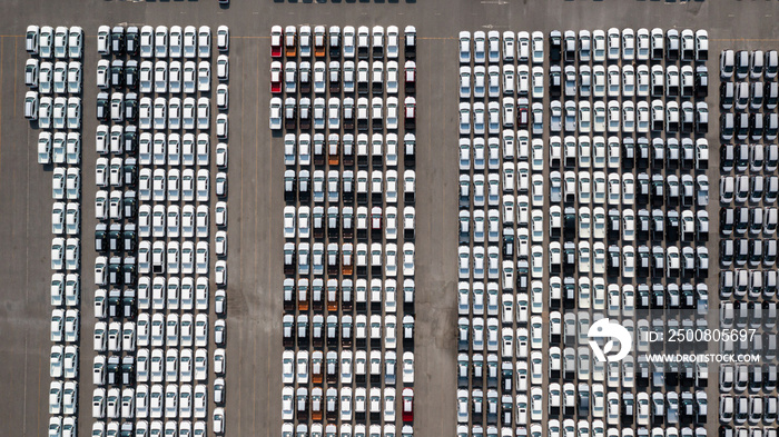 Aerial top view parked new cars at the automotive plant, new car lined up in the port for import and export business logistic to dealership for sale, Automaker distribution center with new vehicles.