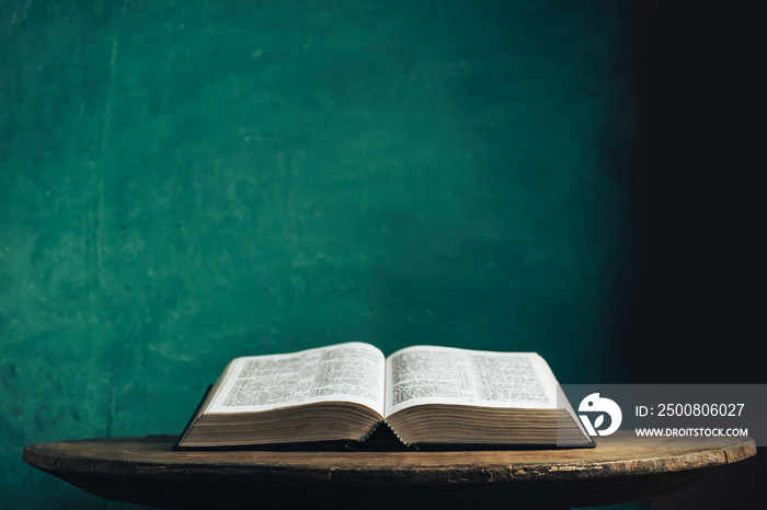 Open Holy Bible on a old round wooden table. Beautiful green wall background.