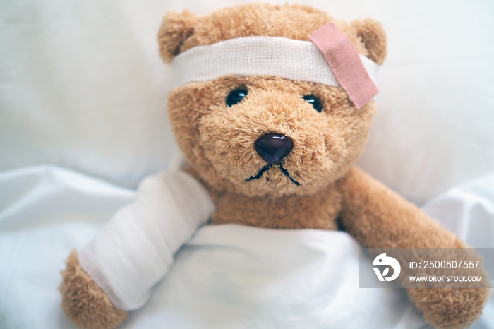 Teddy bear lying sick in bed With a headband and a cloth covered