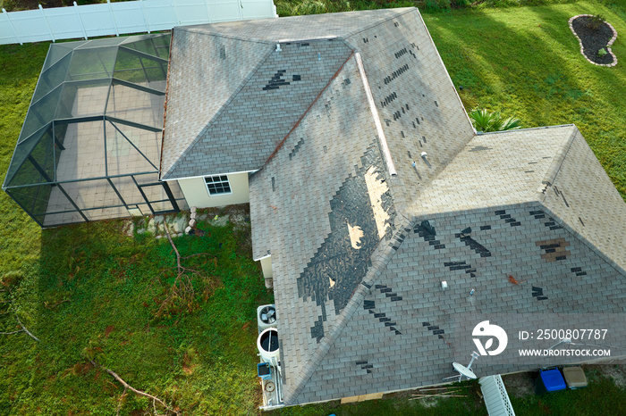 Wind damaged house roof with missing asphalt shingles after hurricane Ian in Florida. Repair of home rooftop concept