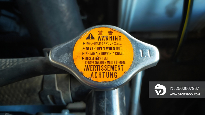 Car radiator cap with warning in many language, in english means translate  never open when hot .