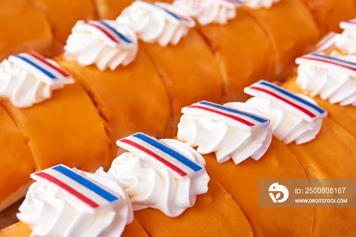 Rows of pastries with orange coloured icing glaze, whipped cream and edible labels with dutch flags on Koningsdag in the Netherlands. A national holiday in the Kingdom of the Netherlands.