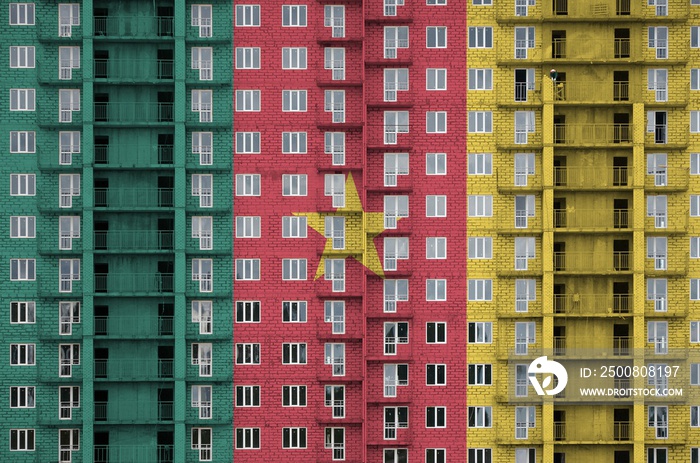 Cameroon flag depicted in paint colors on multi-storey residental building under construction. Textured banner on brick wall background