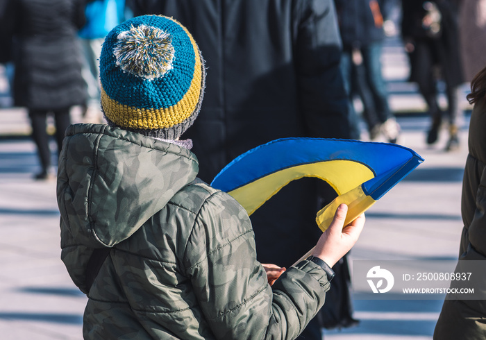 Child or kid with winter clothes, Ukrainian flag and yellow and blue hat, refugee, refugees during war in Ukraine, caused by Putin and Russia