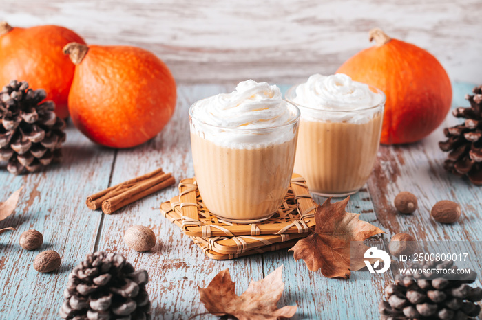 Pumpkin pie smoothie on worn wooden table with cedar cones and dry leaves. Autumn still life with pumpkin smoothie decorated with whipped cream closeup