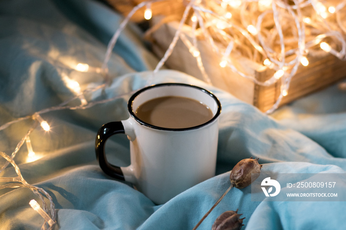 Coffee cup and garland on a bed. Atmospheric hygge style. Cozy winter or autumn concept