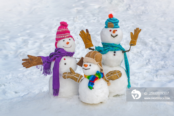 Funny snowman family in stylish hat and scarf on snowy field. Happy winter time. Happy funny snowman in the snow. Happy smiling snowman group on sunny winter day.