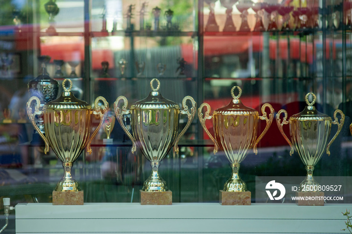 A street view at Trophy cups lined on a shelf throw the window of a shop.