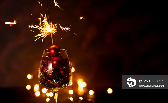 Burning bengal firework in wine glass with red Christmas balls