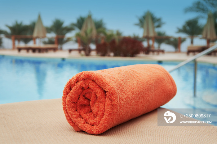 Orange towel lying on a lounger near the swimming hotel pool summer