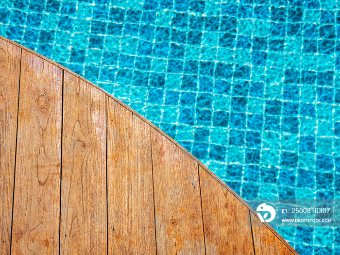 Top view of empty wooden plank table or deck floor curved shape in front of the blurred background of blue mosaic tiles grid pattern in swimming pool. Empty space on poolside, summer background.