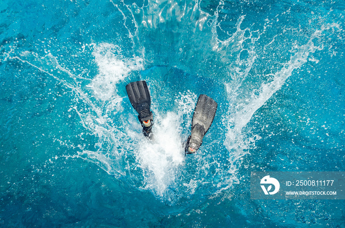 Diver in a wetsuit and flippers jumping in the blue water.