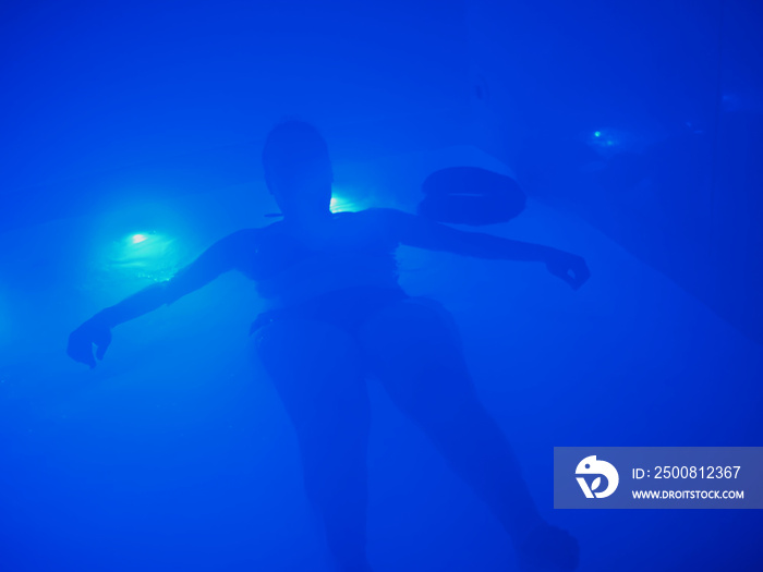Silhouette of a woman in a floatation bath, blue atmosphere.