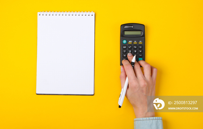 Economic analysis. Female hands use calculator on a yellow background with a notebook. Top view