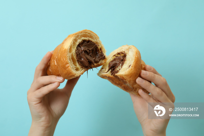 Female hands holds croissant with chocolate on blue background