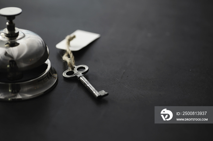 A shiny silver metal bell at the hotel reception. A table in the hotel at the concierge with a bell and a door key. Key and bell in a hotel.