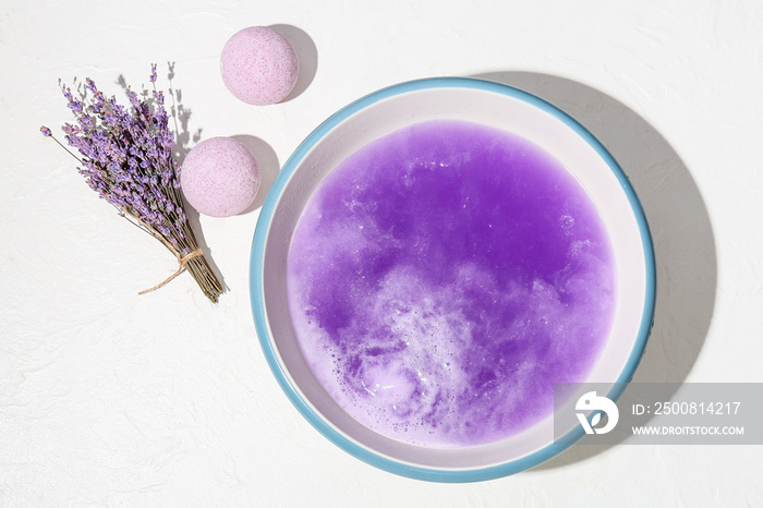 Bright bath bomb dissolving in bowl with water on light background