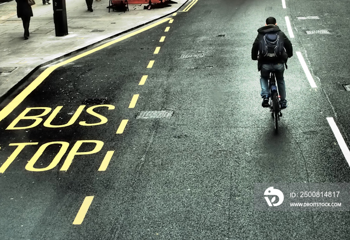 A bus stop sign on the road and a cyclist on the streets of London.