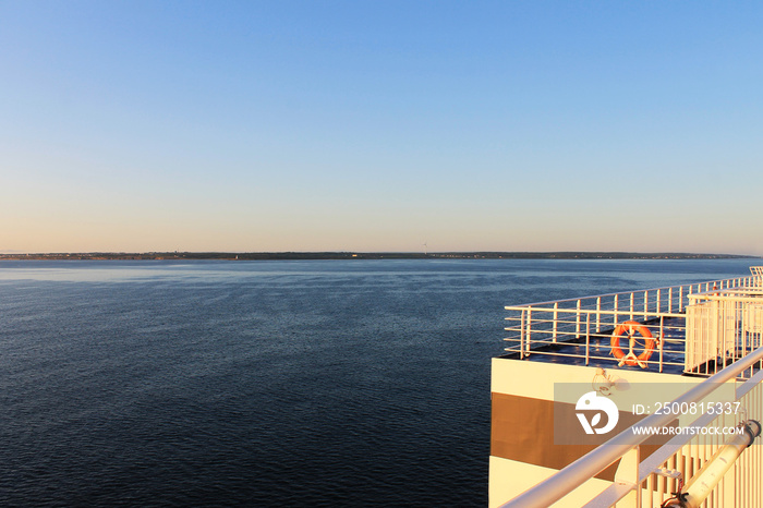 Top deck of a ship at sea, early morning. Morning sun, ocean in the background, land just visible on the horizon.