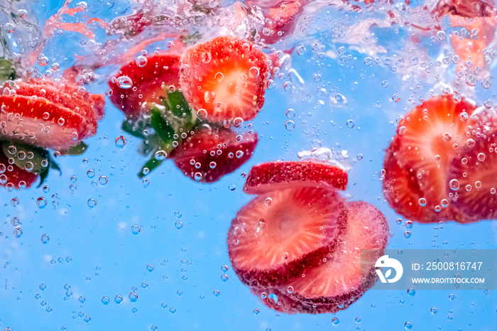 Sliced Strawberry in water with water splash and air bubbles on blue background. Close up image.