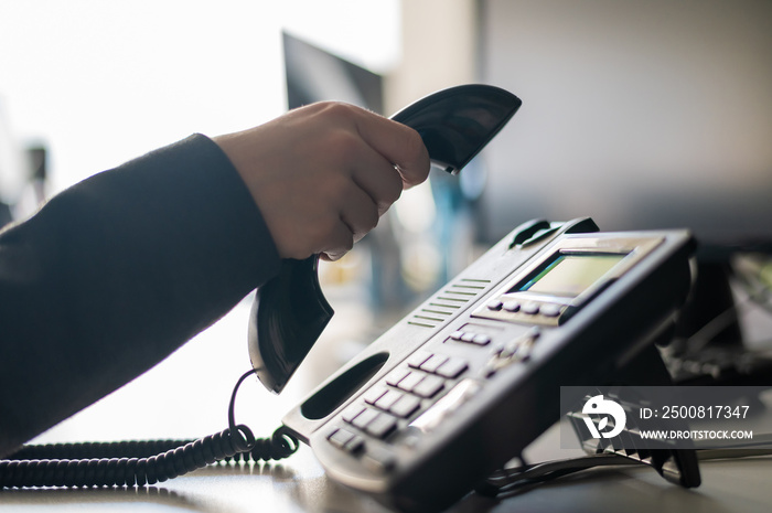 Close-up of the hand of a female office worker dialing a number on a landline phone. Faceless woman secretary calls on the phone