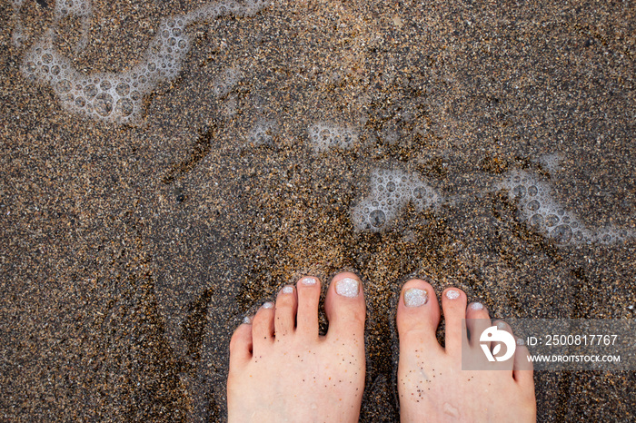 Wrinkled and sandy feet of a woman after playing in the water on a sandy beach background.