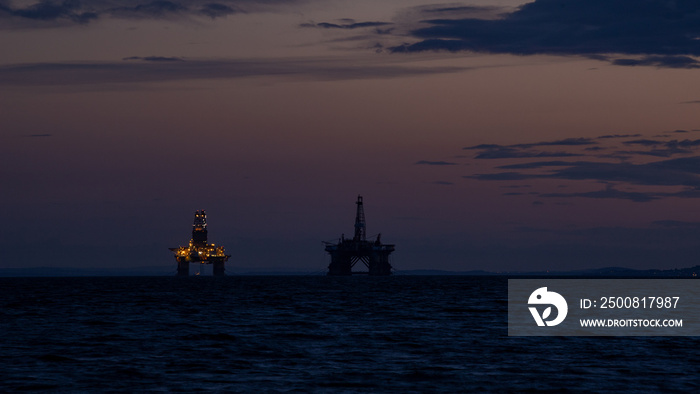 Oil rigs of the coast of Scotland, illuminated by their lights as the sun sets