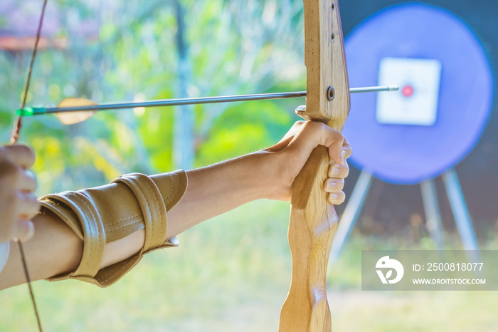 Tourists try to use a bow and arrow and shoot at a target in the amusement park.