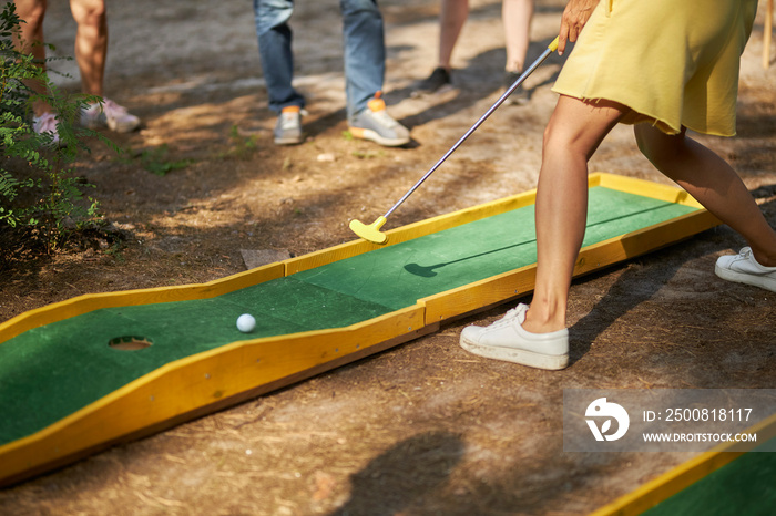 mini golf in nature. minigolf player with white sneakers putting golf ball into the hole on bumpy green lane.