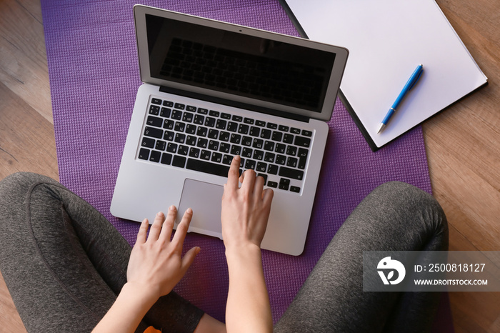 Young sporty woman with laptop sitting on yoga mat. Concept of balance between rest and work