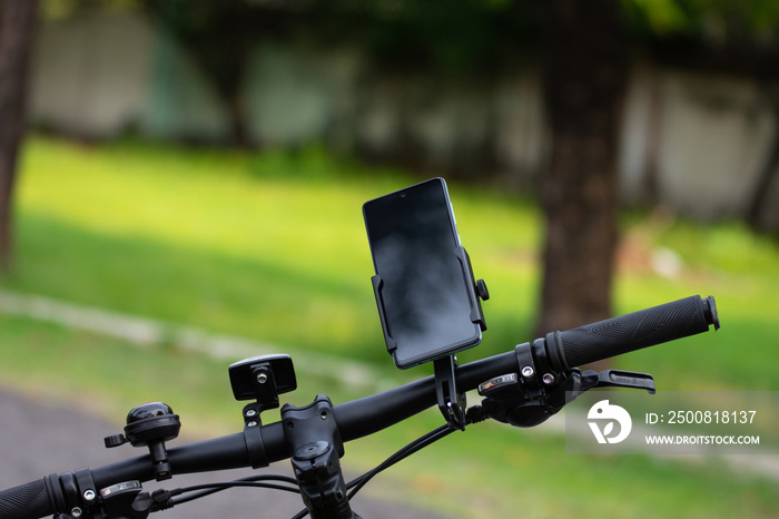 Smartphone attached on mount rack to the handlebars of the bicycle on blurred background.