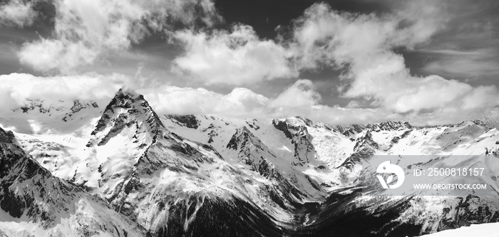 Black and white panorama of snowy winter mountain in sunlight clouds