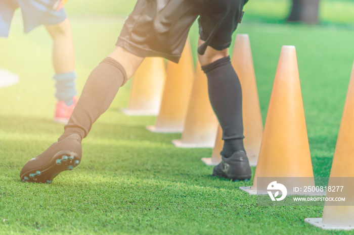 Children feet with soccer boots training on training cone on soccer ground